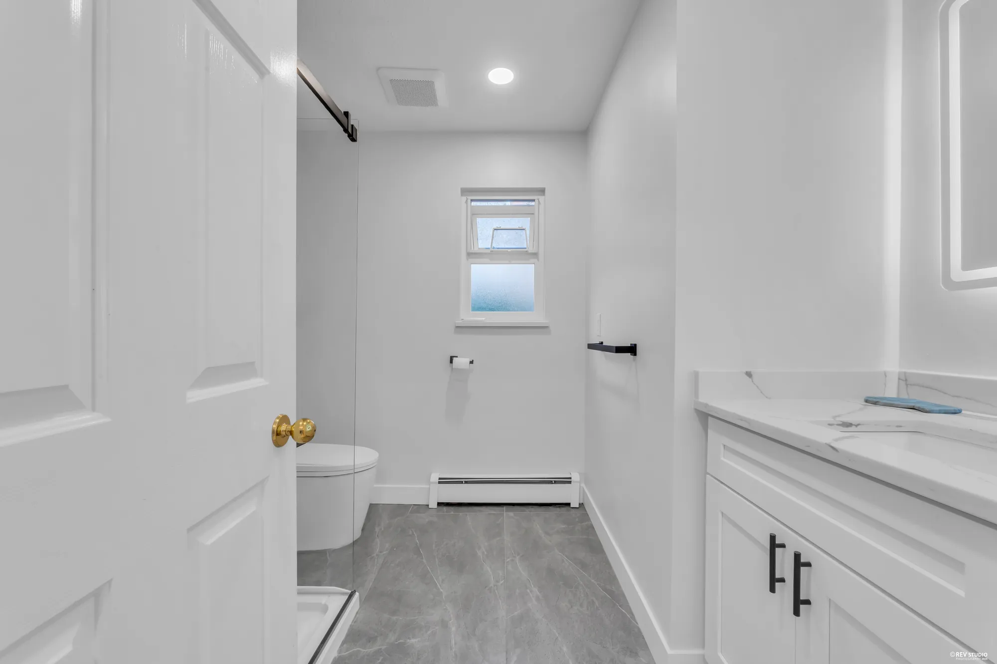 The main-floor bathroom, renovated in white: a barn door, a grey tile floor, a white vanity, a window