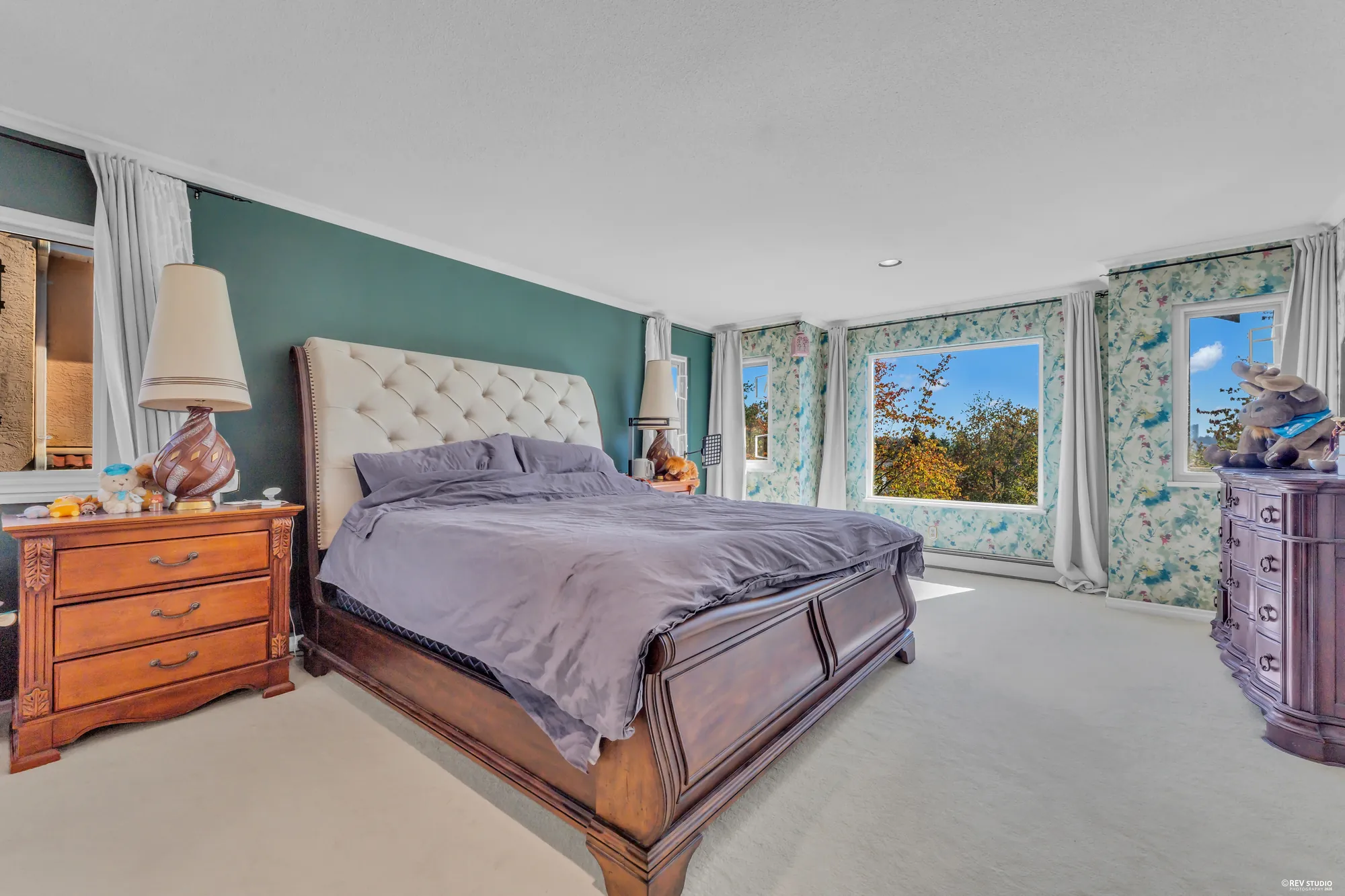 A bedroom with a green accent wall and floral wallpaper, a sleigh bed, windows on two sides