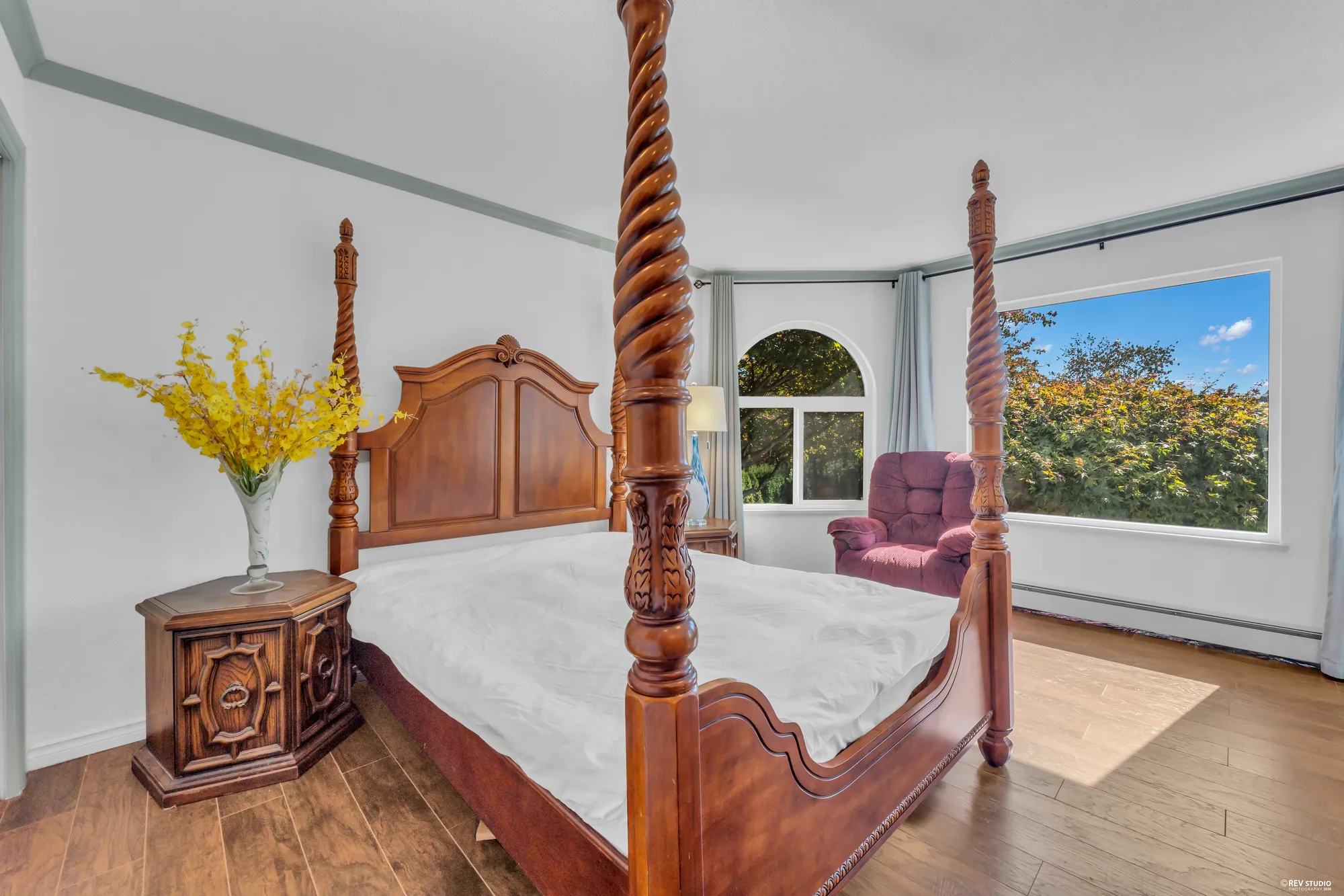 The main-floor bedroom: a four-poster bed on hardwood, an arched window and the bay to the front