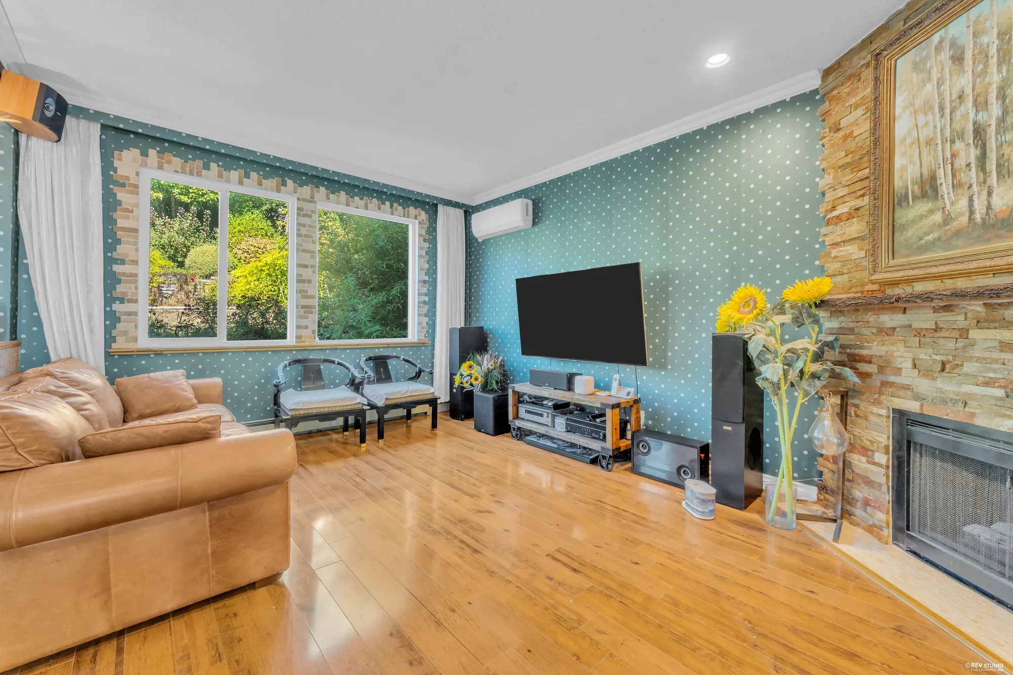The family room: leather sofas on hardwood, a stone fireplace with a television beside it, the windows to the garden