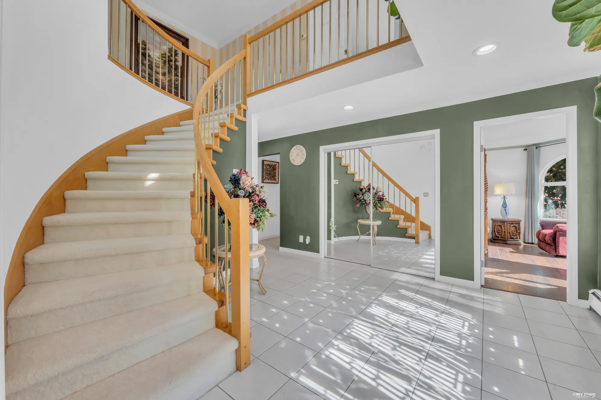 The foyer: a curved oak stair rising under a double-height ceiling, the tile floor, the living room and dining room through the arches