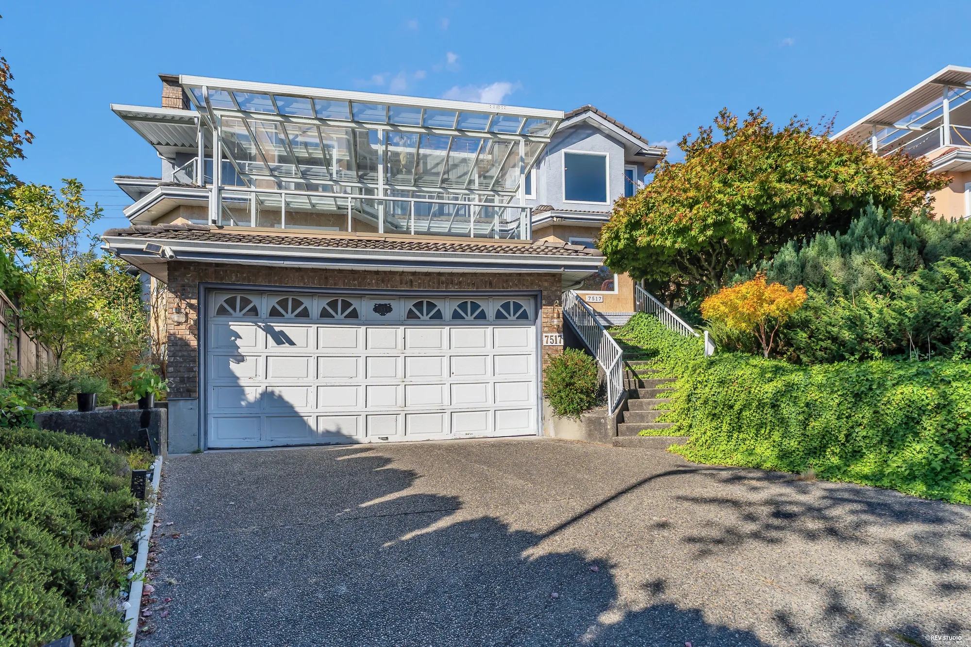 The double garage at the street, the glass roof of the terrace over it, the stair up beside the garage, shrubs either side