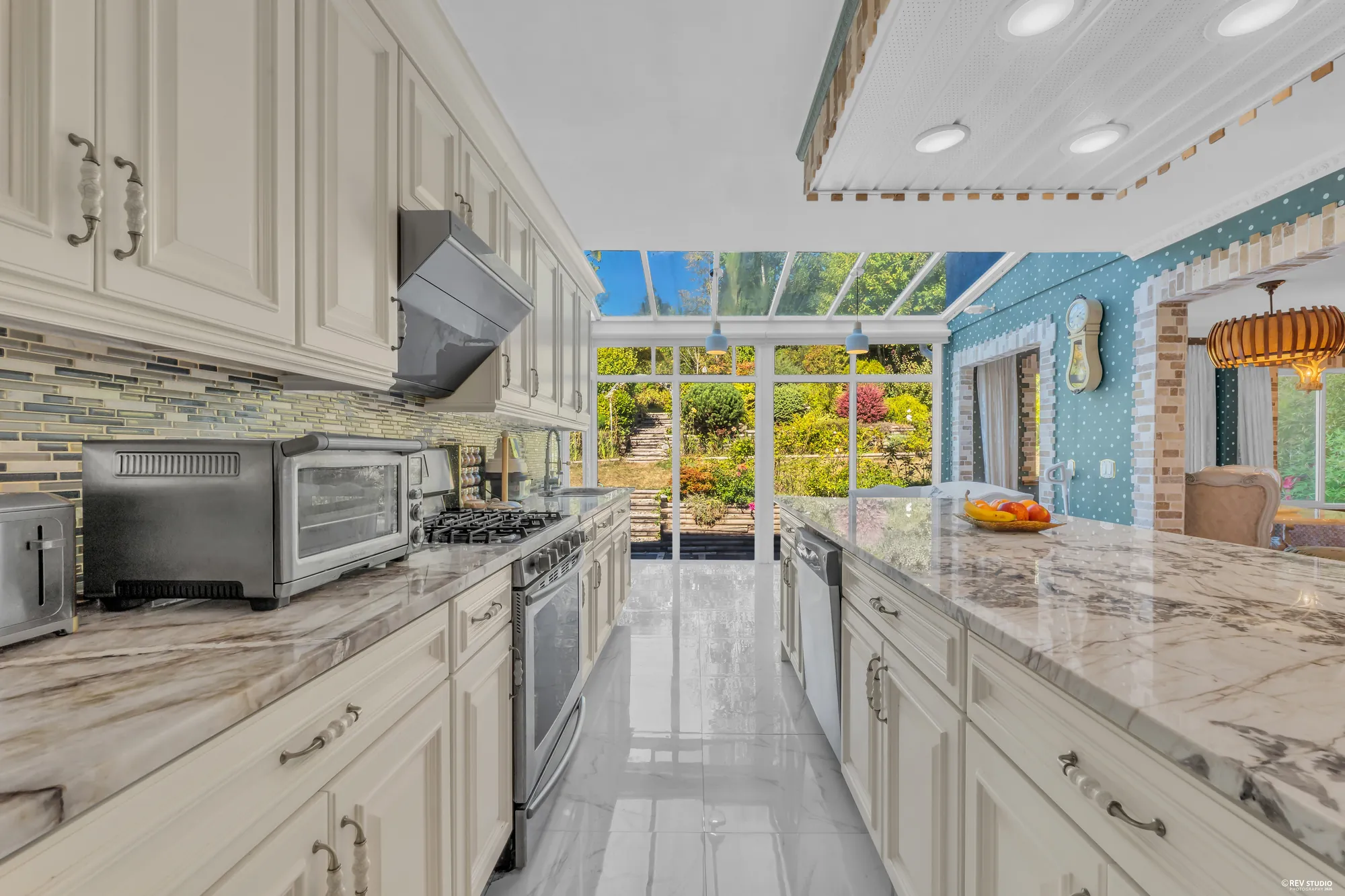 The range wall: a stainless range under the hood, the tile backsplash, the glass roof beyond