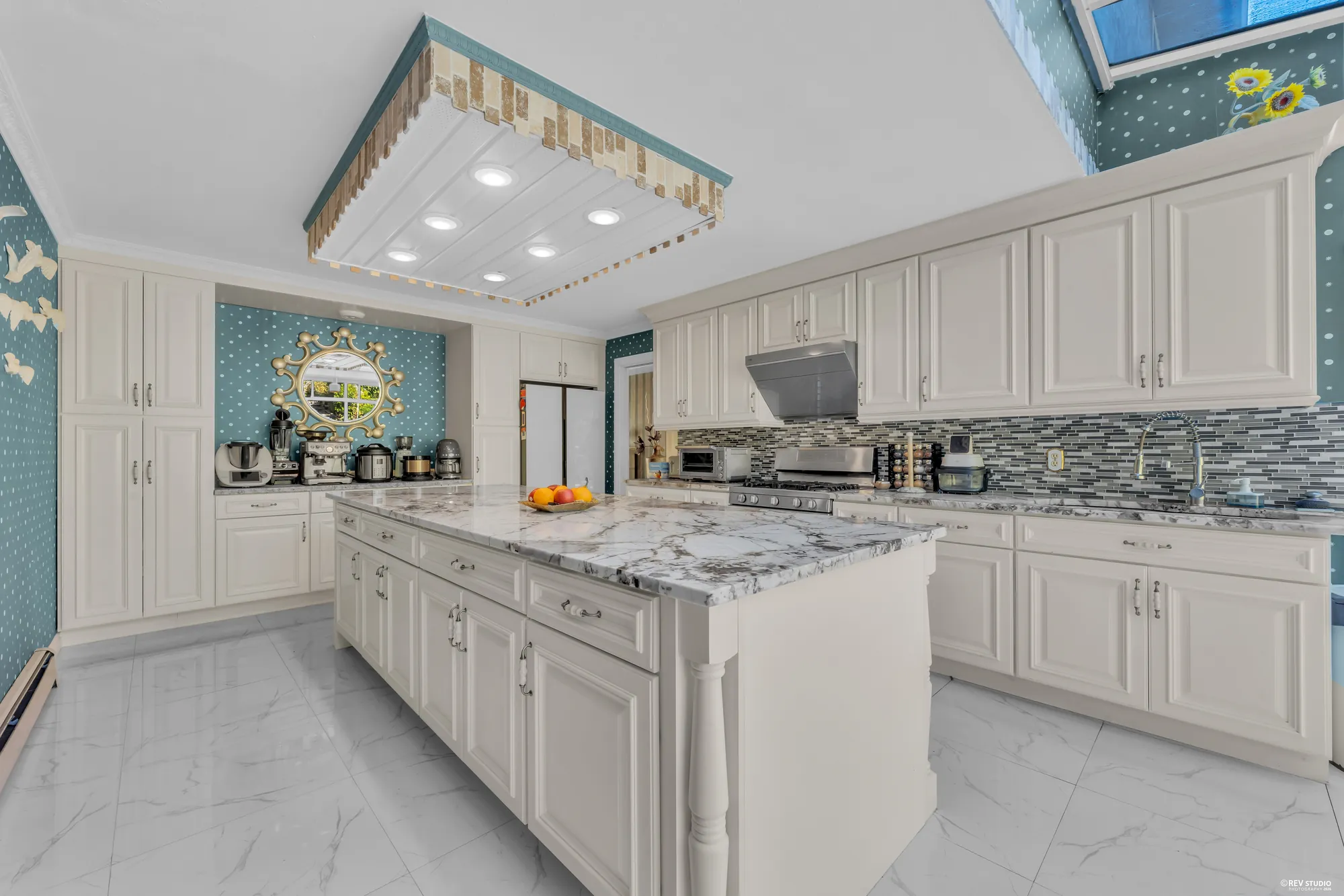 The far end of the kitchen: a wall of white cabinets, the marble counter, a coffee corner under the skylight