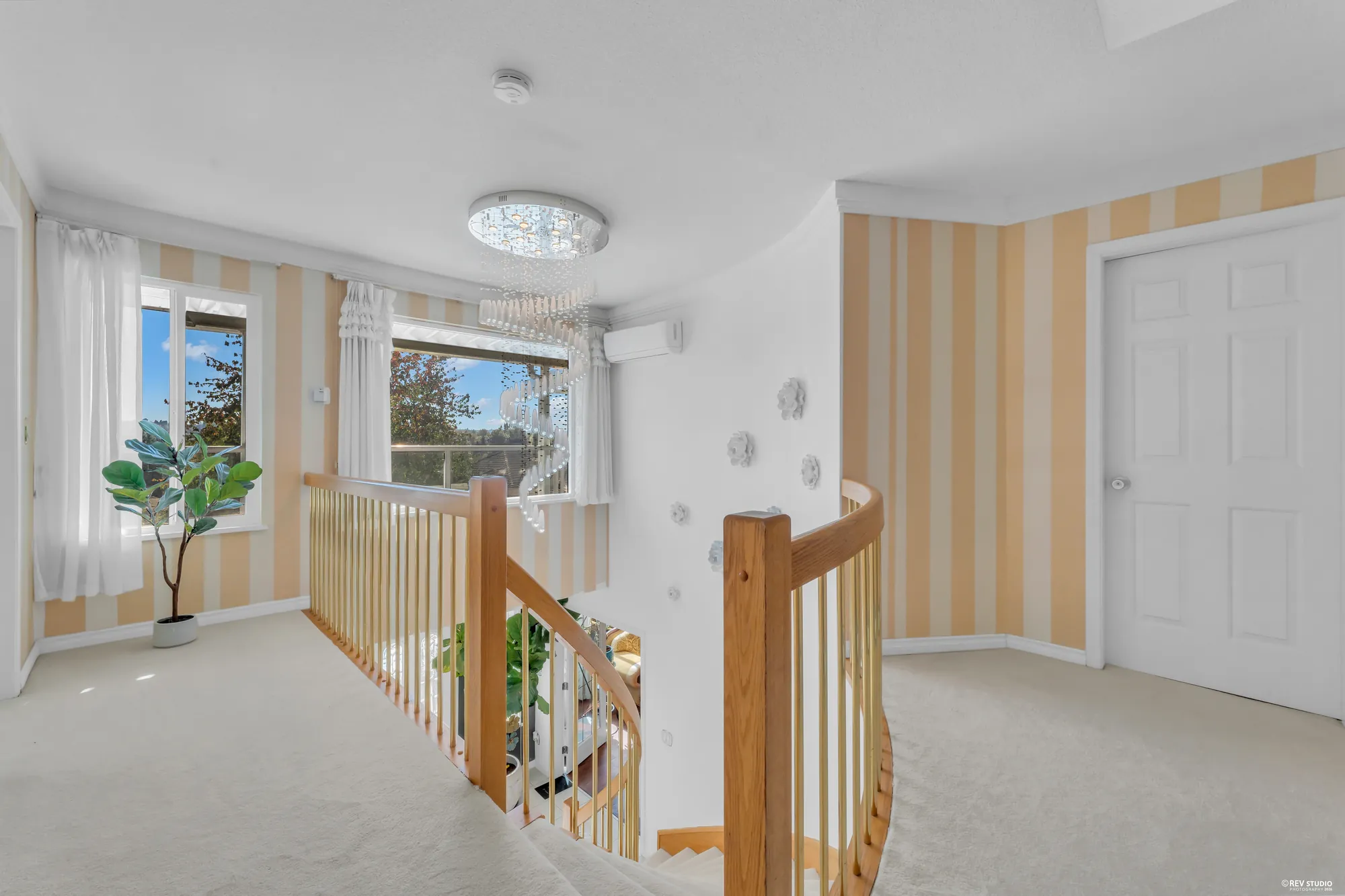 The upper landing: the oak rail of the curved stair, a chandelier, striped wallpaper, windows to the front