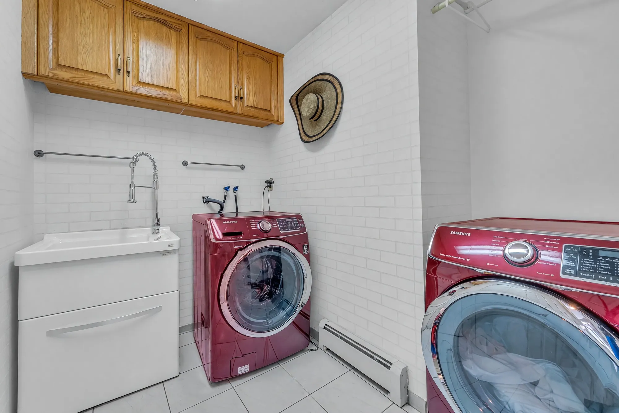 The laundry: oak cabinets over a sink, a front-loading washer and dryer, white tile walls