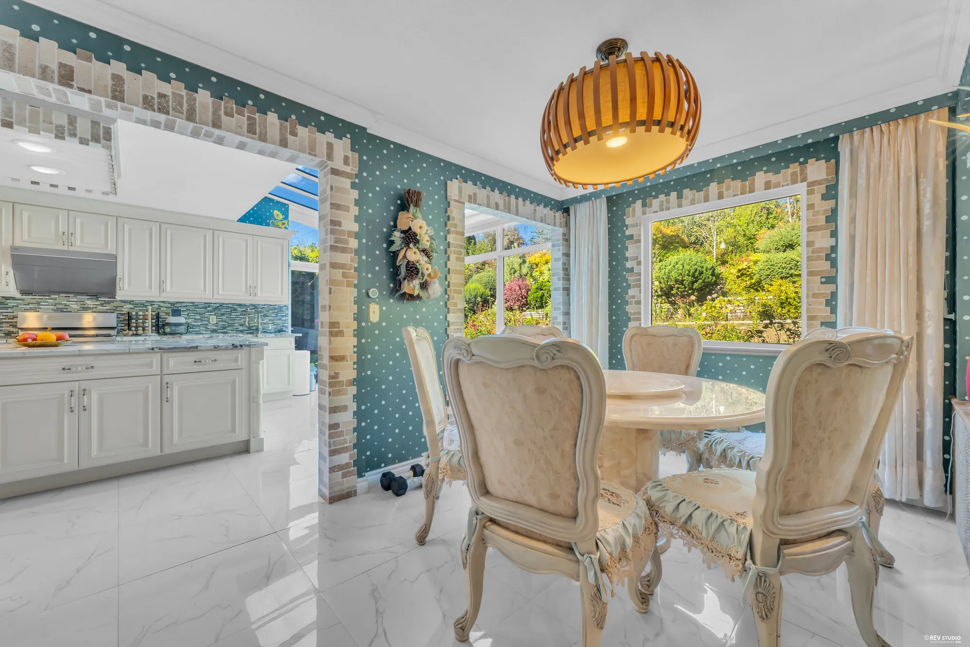 The breakfast nook under its glass roof: a round table and chairs by the windows to the garden, a pendant above