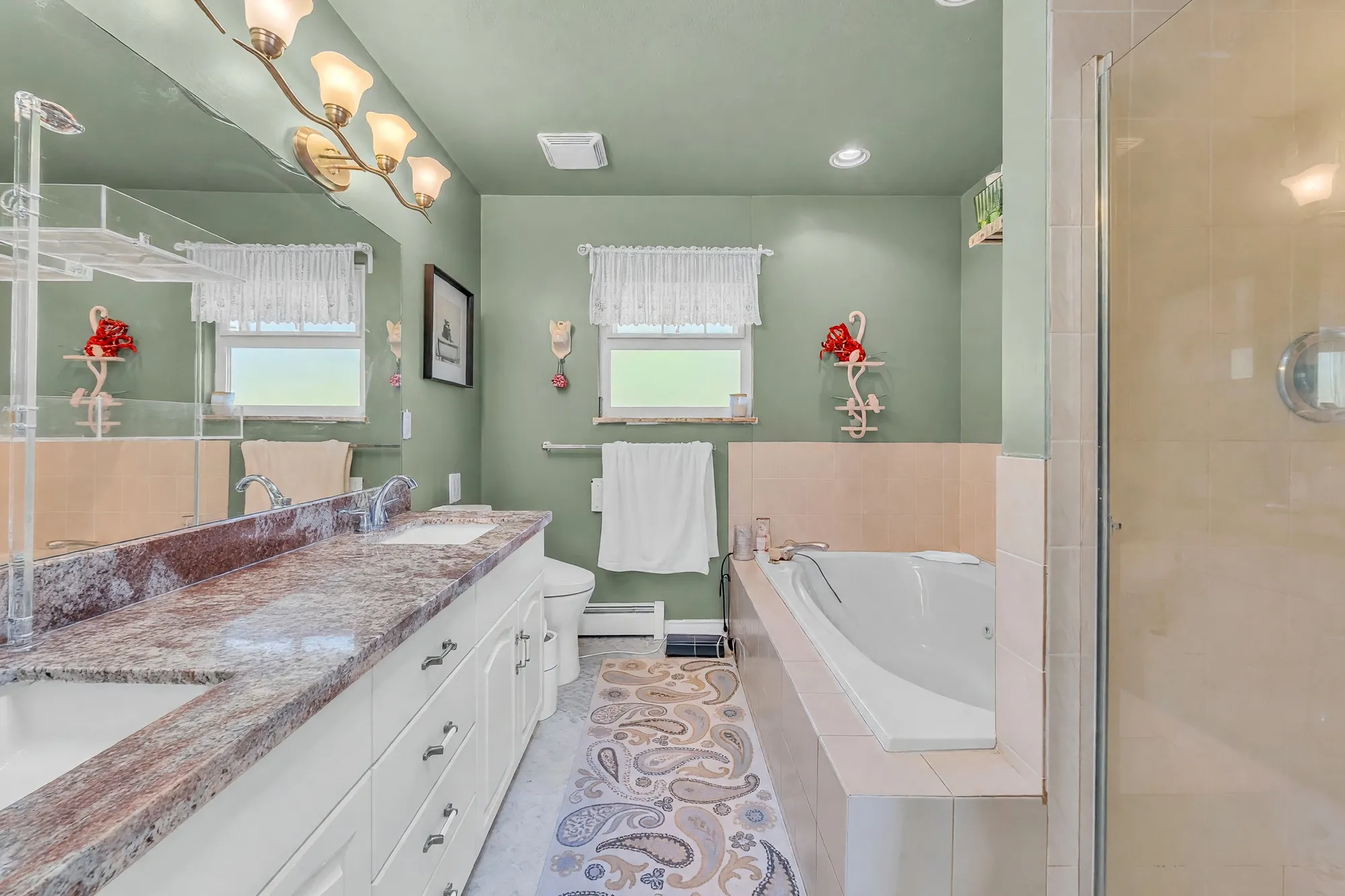 The primary bathroom: a long granite vanity, a soaker tub under a window, a glass shower