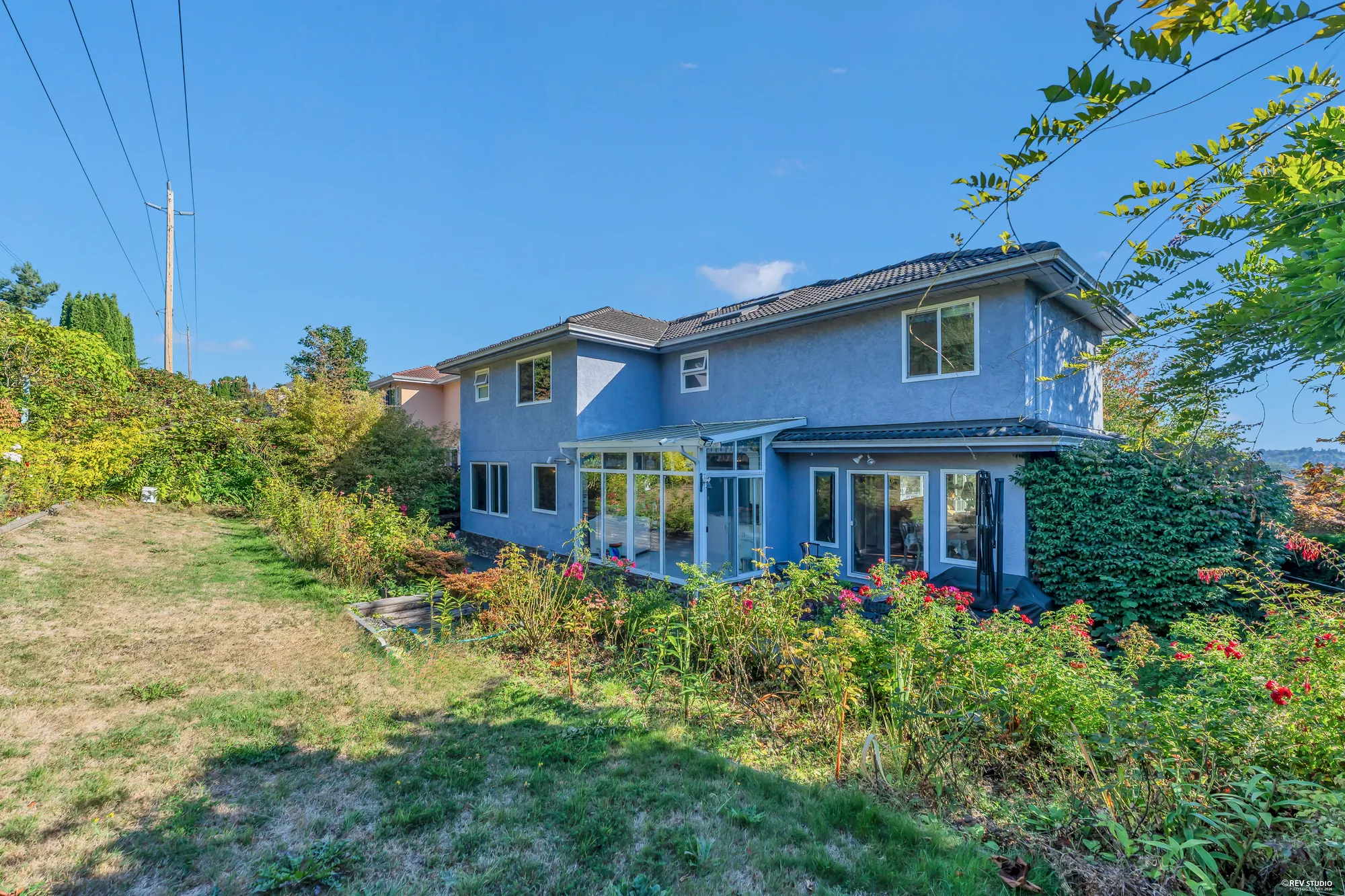 The back from across the lawn, the patio furniture under the glass sunroom, the trees at the edge