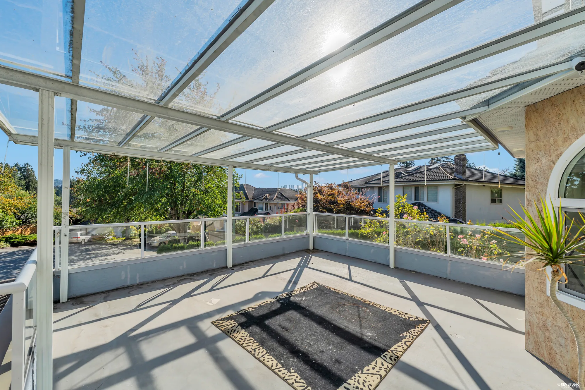 The glass-roofed terrace over the garage: a wide deck under a glass roof on white posts, a rug at its centre, the street side open