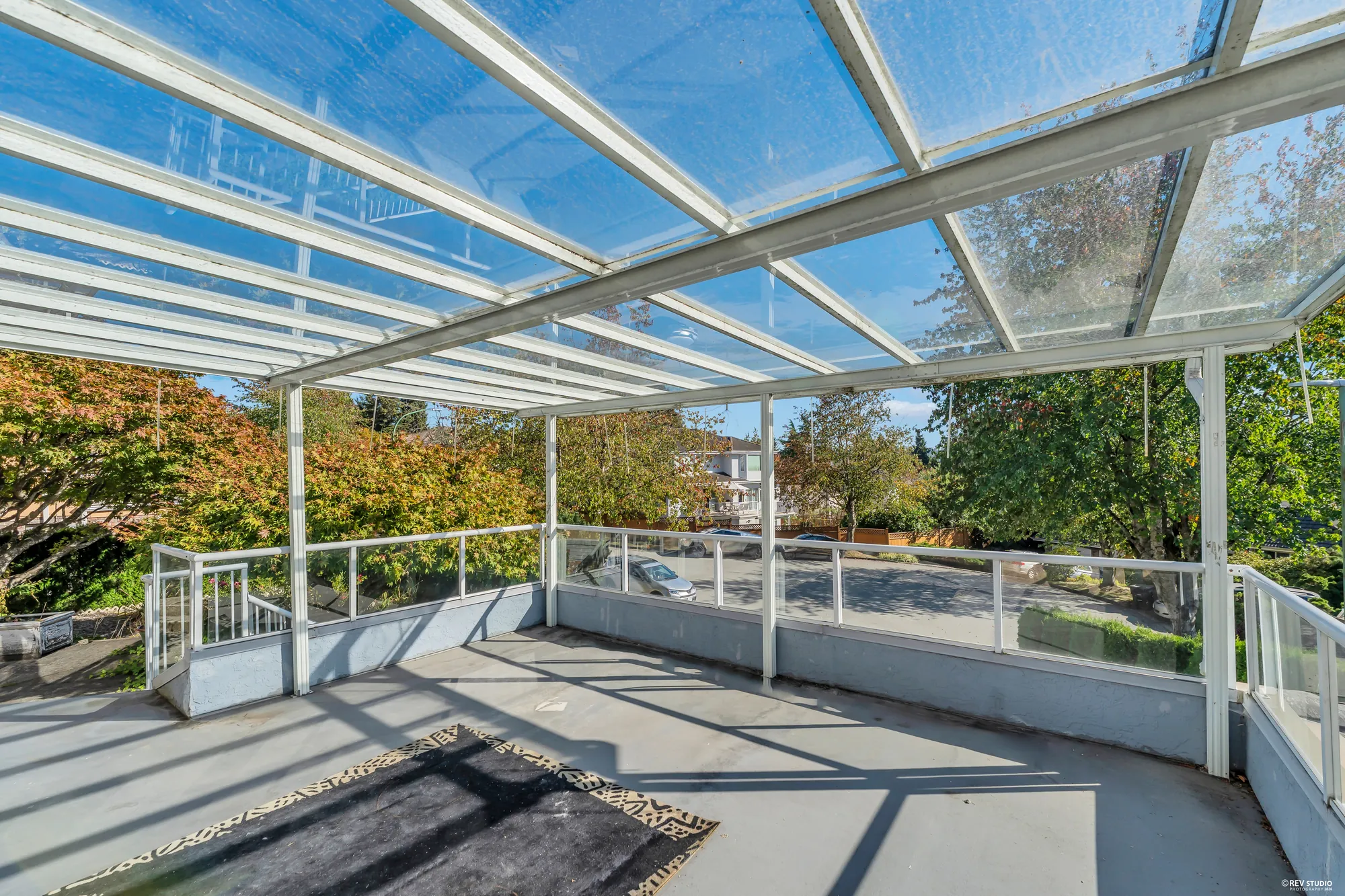 The terrace toward the street, the glass roof overhead, the neighbours' roofs beyond the railing